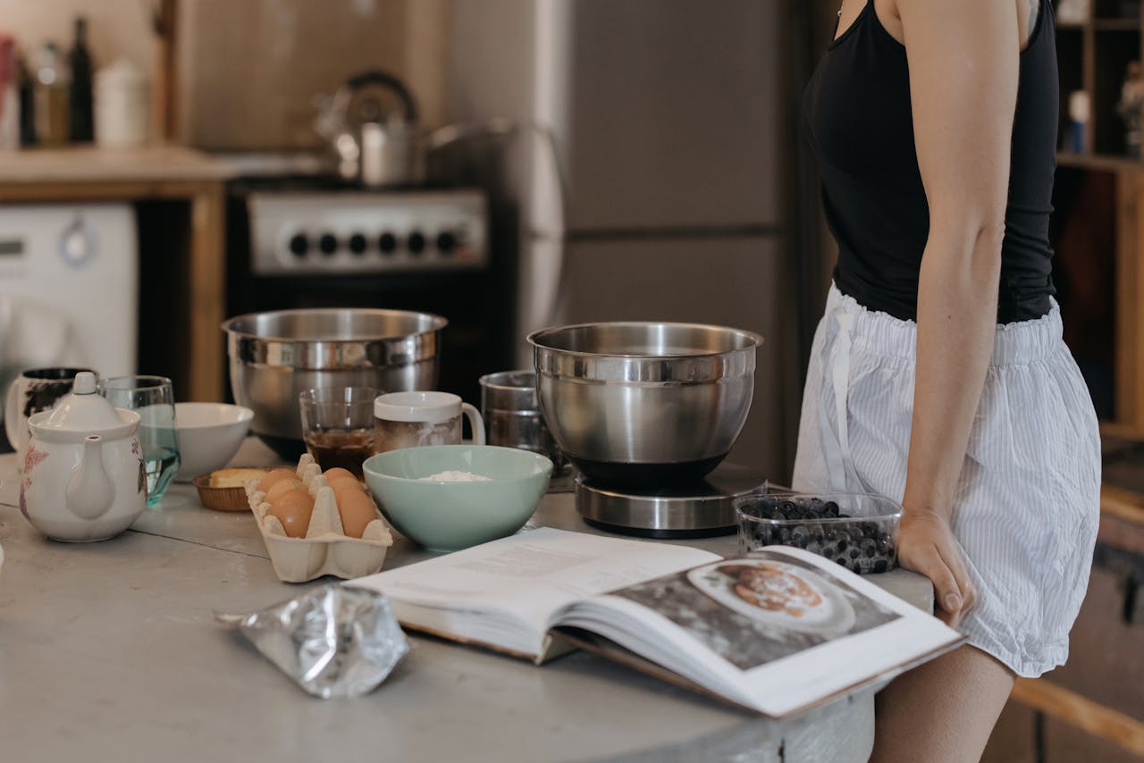 Home Woman in kitchen preparing breakfast with various ingredients and a recipe book open.