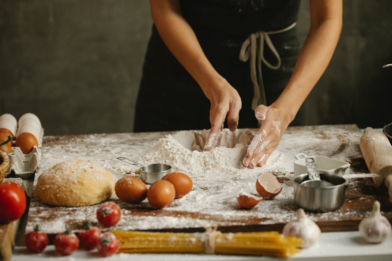 Home Unrecognizable woman in apron making dough with eggs and flour on chopping board on table with cooking ingredients on kitchen
